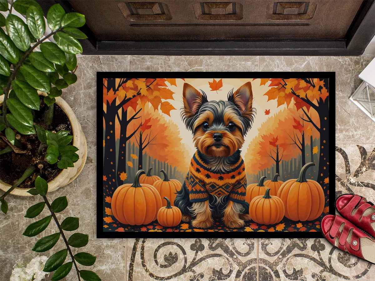 Decorative doormat with a dog wearing a sweater and pumpkins in an autumn setting on a patterned floor.