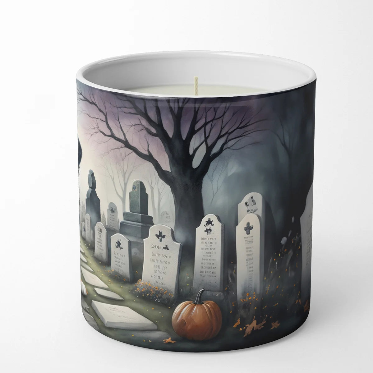 Candle with a Halloween-themed design of gravestones, pumpkins, and a tree on a white background.