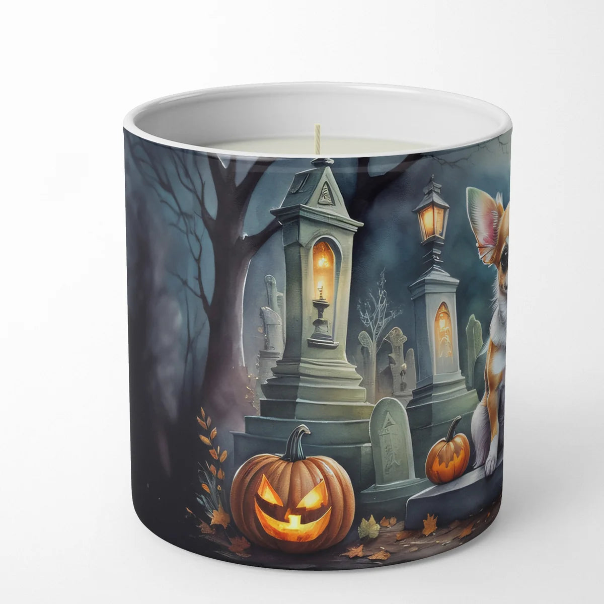 A white ceramic candle jar featuring a detailed Halloween-themed illustration on the outside. The artwork depicts a spooky graveyard scene with a carved jack-o'-lantern pumpkin, tombstones, a lit streetlamp, bare trees, and a white cat on the right side.