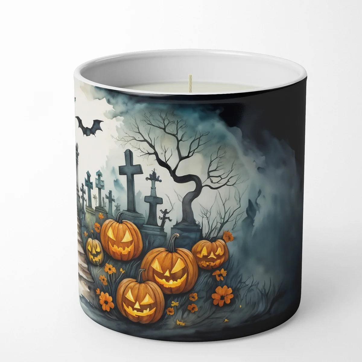A white candle in a cylindrical ceramic container with a Halloween-themed wraparound illustration featuring carved pumpkins, tombstones, a bare tree, bats, and fog on a light gray background.