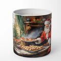 A white ceramic candle in a cylindrical mug-style container, featuring a printed illustration of Santa Claus serving pastries in a cozy holiday kitchen scene.