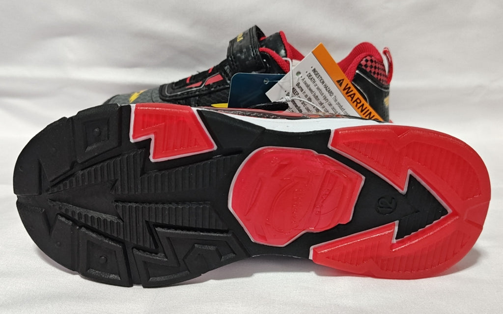 A close-up of a sneaker's outsole, showing a black treaded design with prominent red sections, alongside the upper shoe in gray, black, red, and white with retail tags attached.