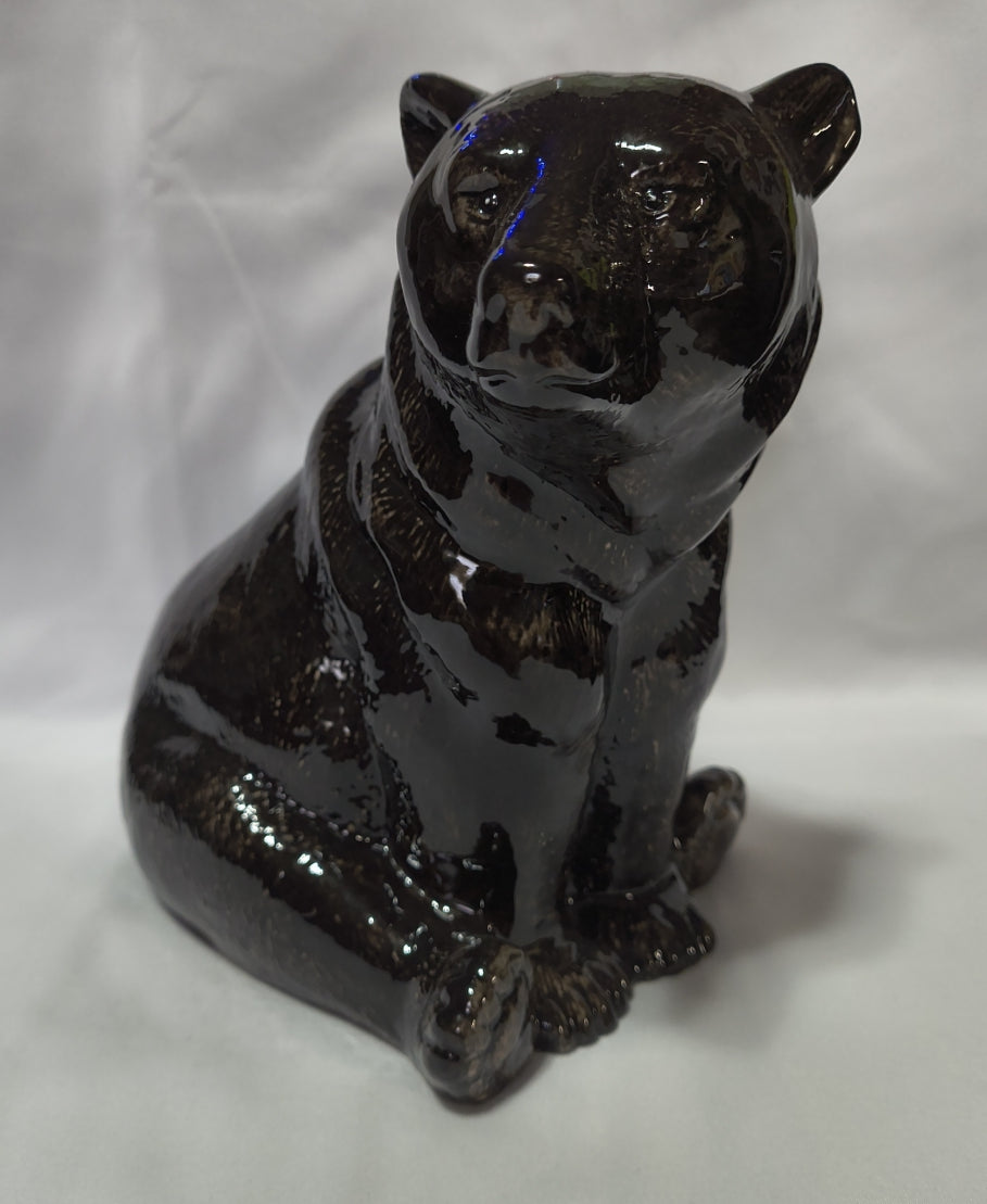 A glossy black ceramic bank of a black bear, shown from a high-angle perspective on a white fabric background.