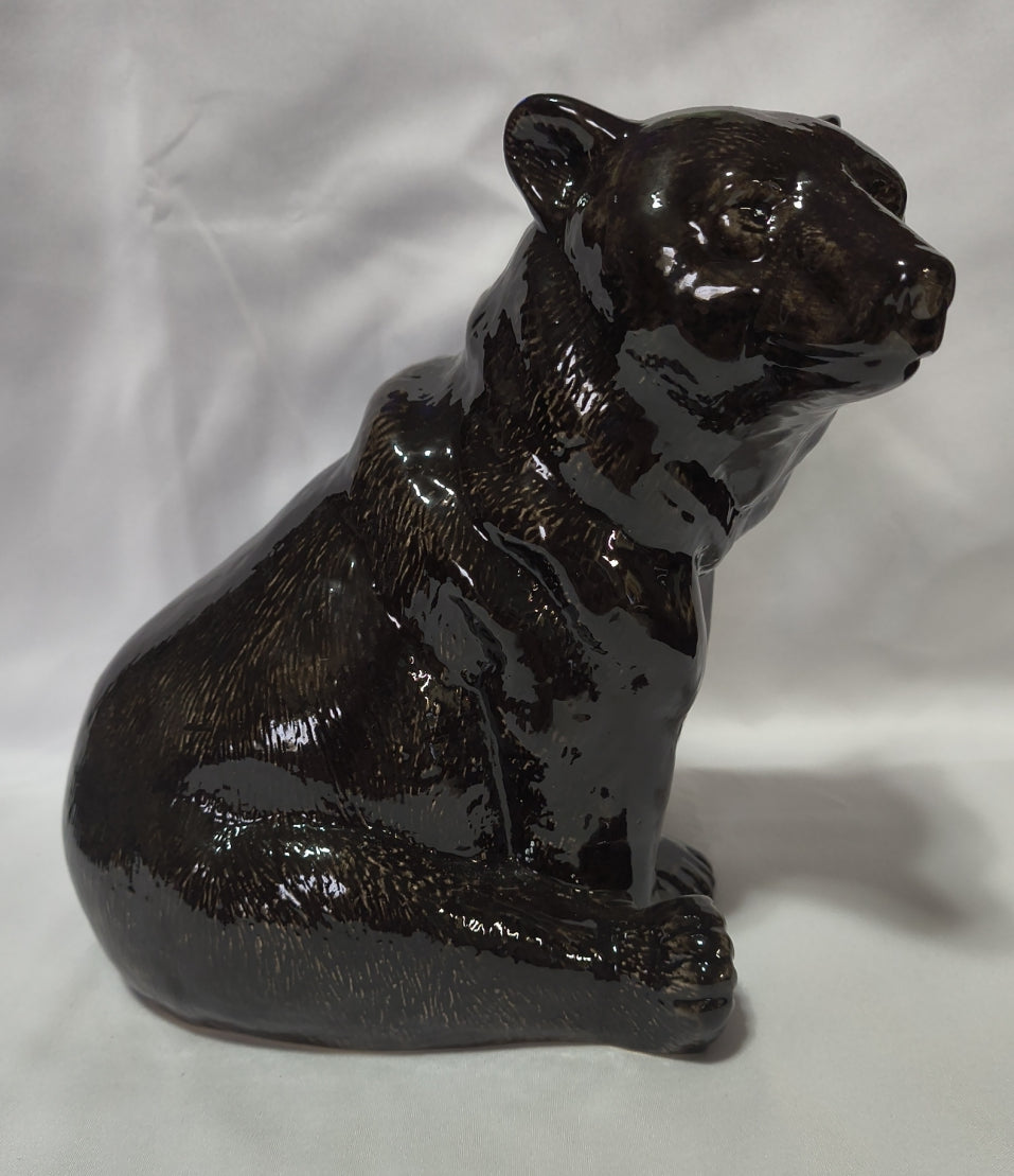 A glossy black ceramic bank of a black bear, shown against a white fabric background.