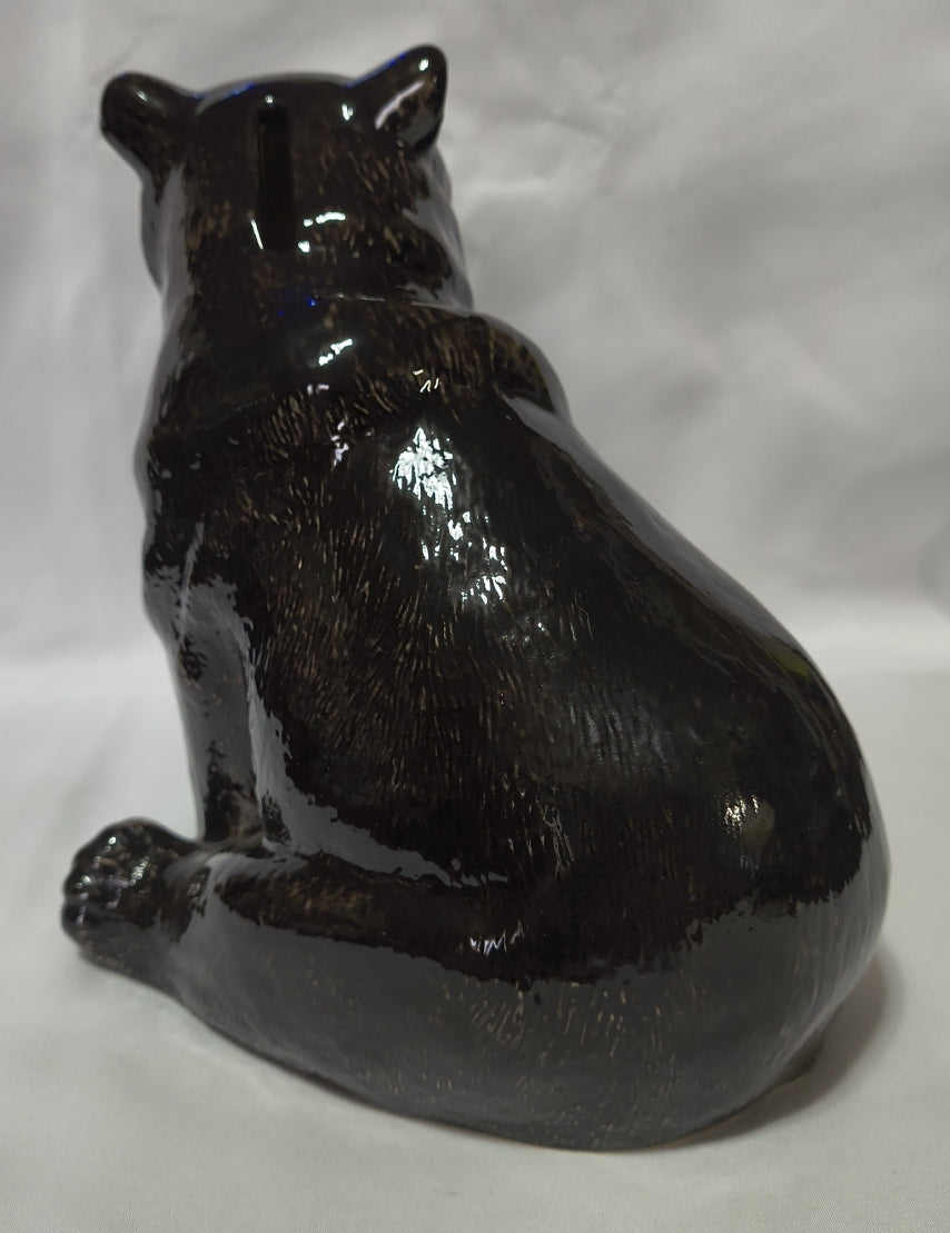 A glossy black bear bank posed sitting, photographed against a wrinkled white fabric background.