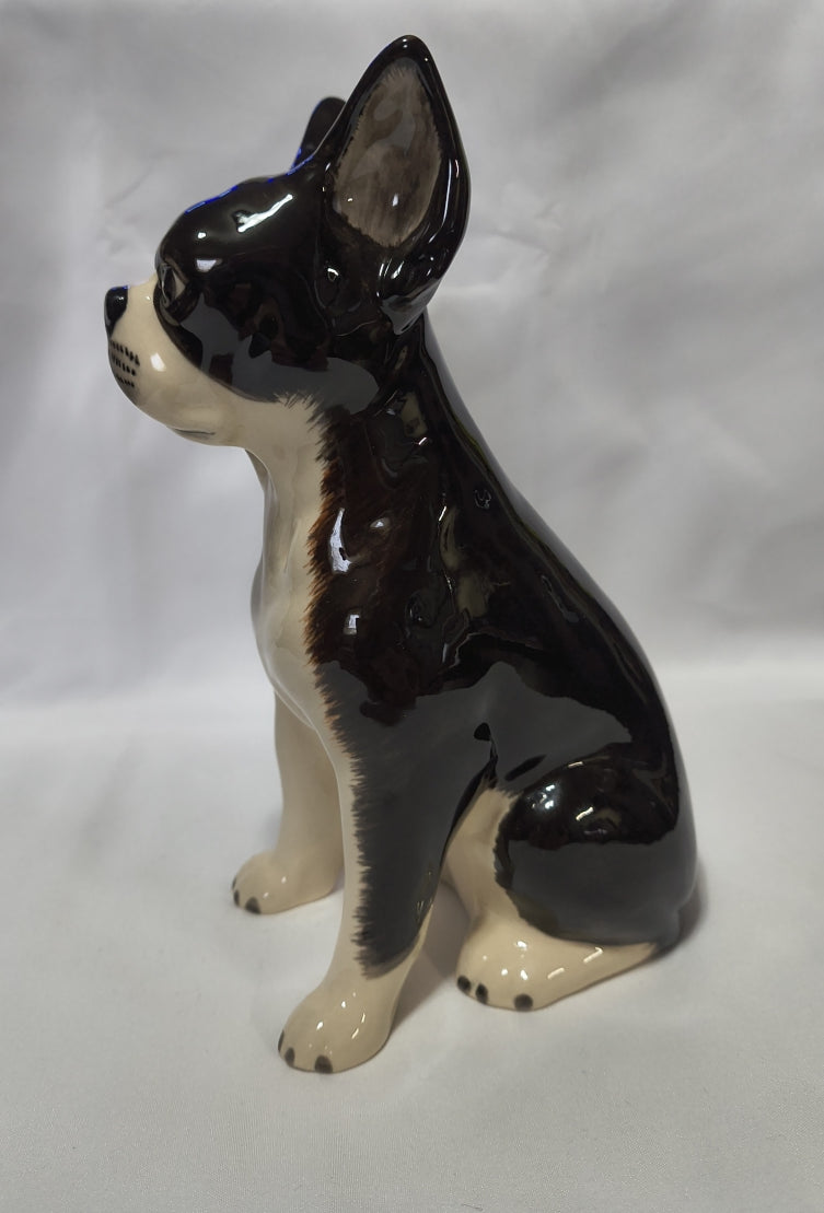 A ceramic hand-painted Boston Terrier Bank, shown from a side profile against a white fabric background.