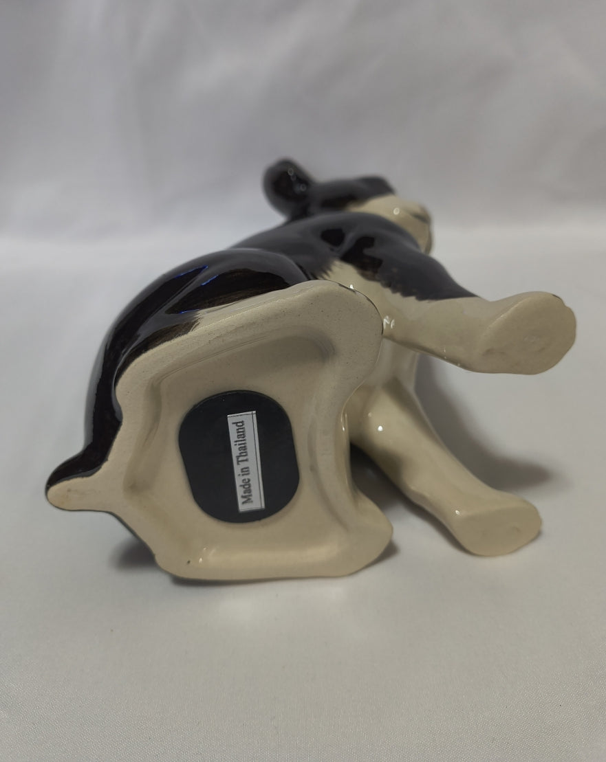 A ceramic bank lying on its side, featuring a glossy black body and a cream-colored underside with a small 'Made in Thailand' label.