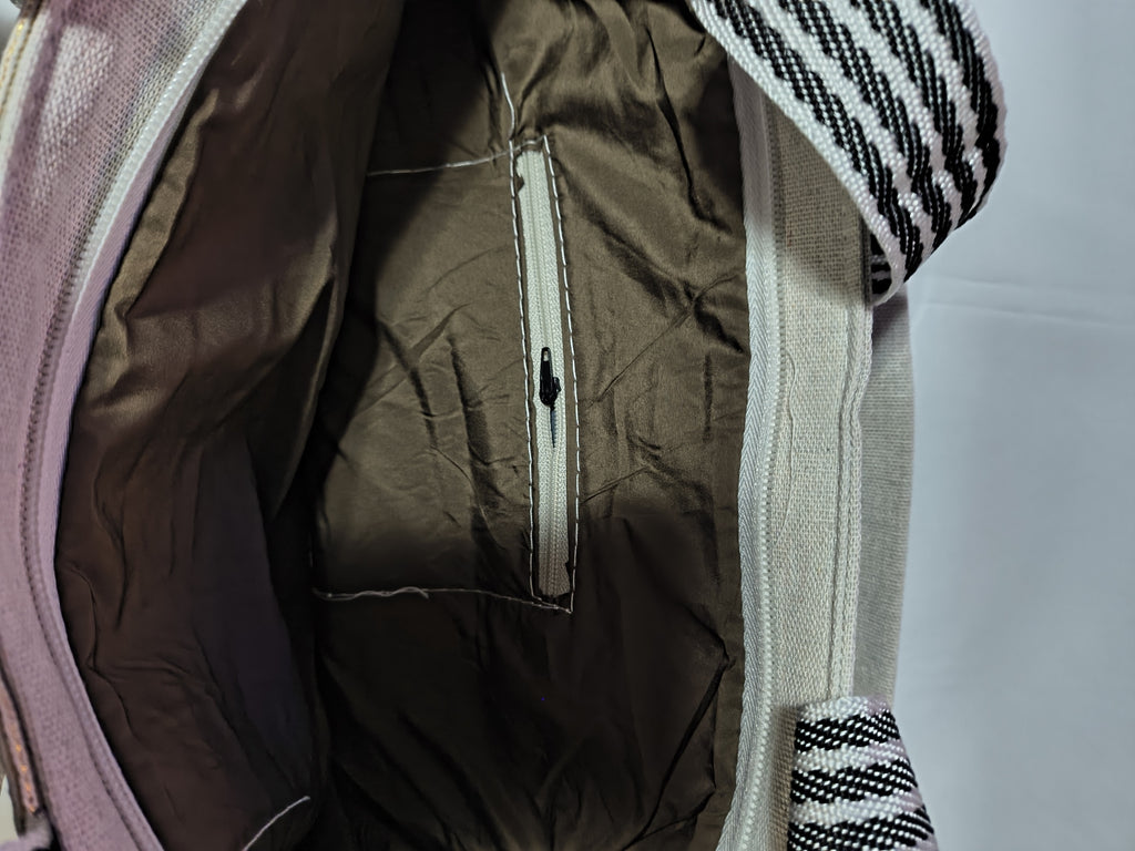 Close-up of the interior of a canvas bag, showing a dark brown inner pocket with a white zipper, and a striped woven strap.