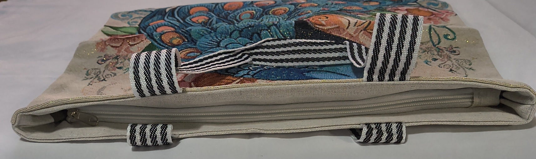 A canvas tote bag with a colorful peacock illustration on the front and striped woven handles, photographed on a white fabric background.