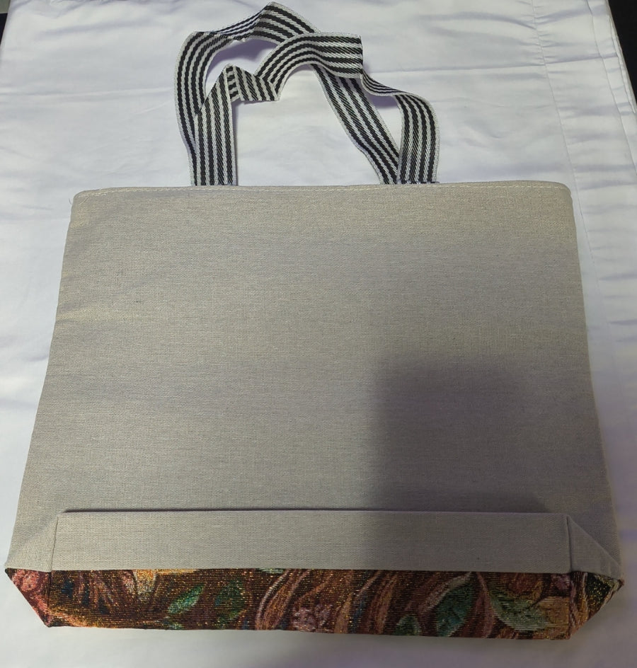 A light beige back of a canvas tote bag with black and white striped handles, laid flat on a white fabric background.