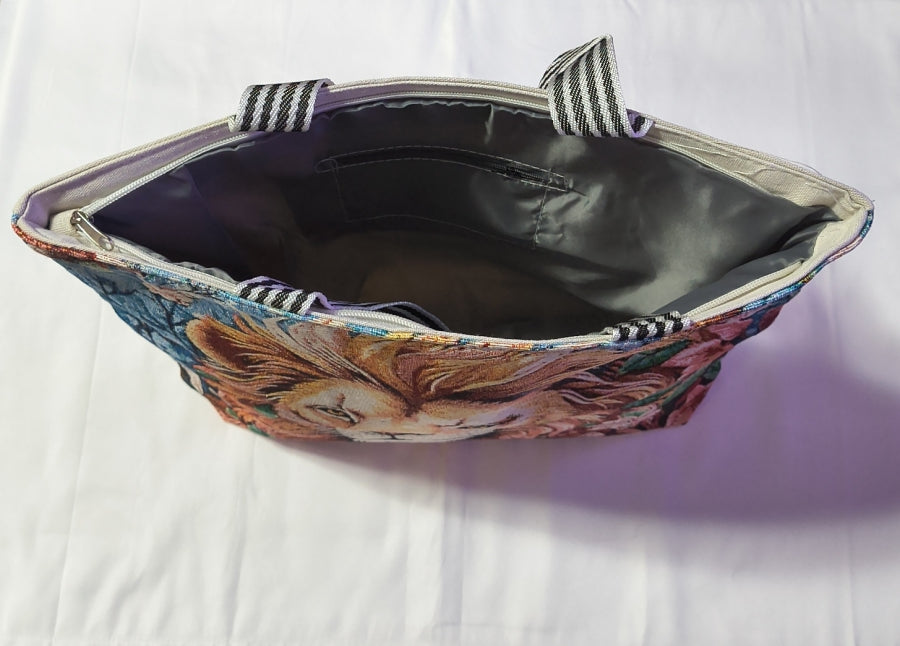 A canvas tote bag with a colorful lion print on the exterior and a gray interior lining, shown open on a white fabric background.