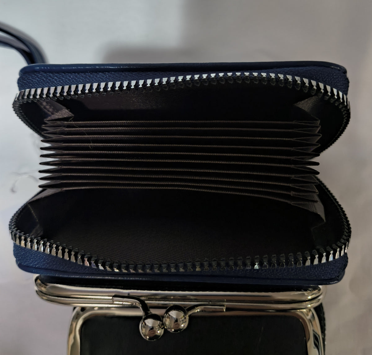 A navy blue zip-around wallet with multiple card slots, shown open to display its interior capacity. The wallet features a silver-tone metal zipper and a silver-tone kiss-lock clasp at the bottom.