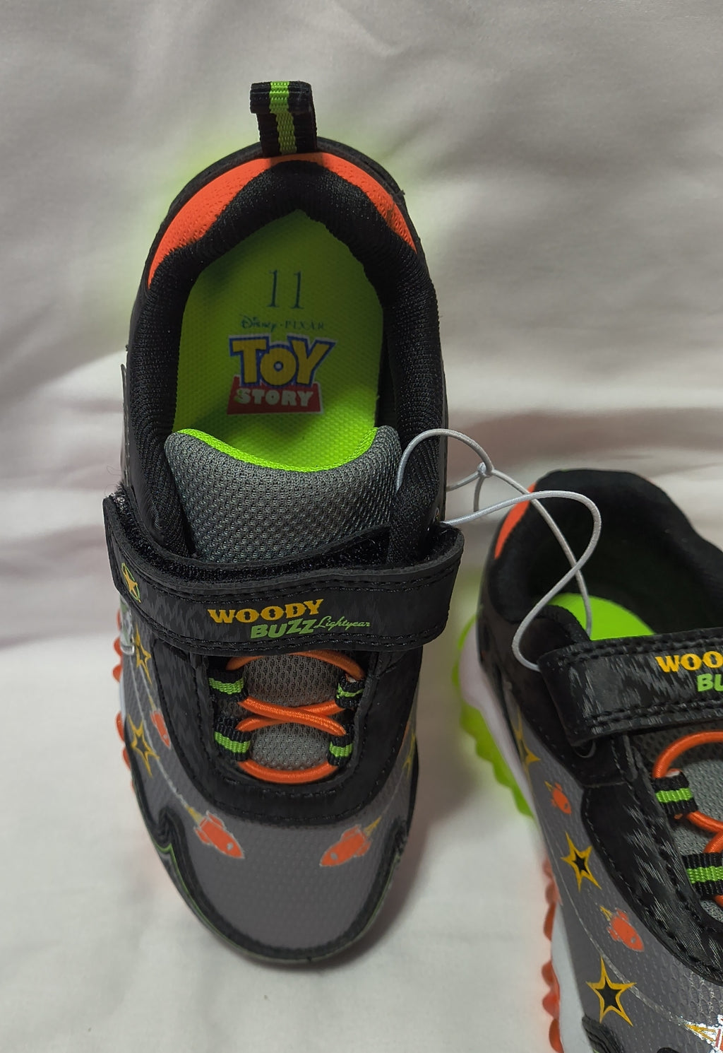 A pair of children's Toy Story shoes in black, gray, and neon green, featuring Woody-themed strap details and character graphics.