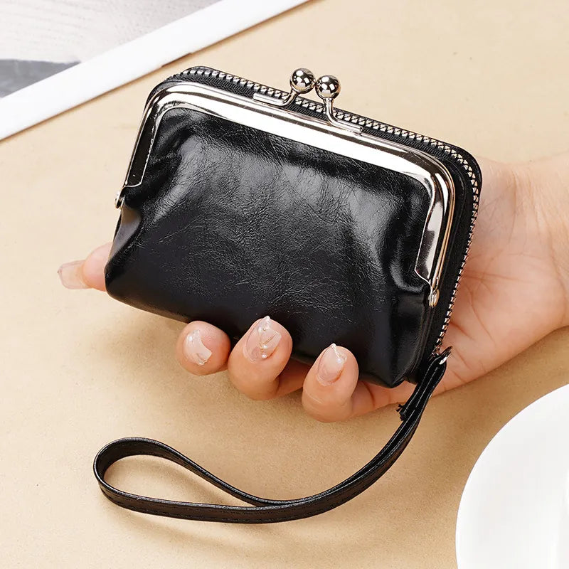 Hand holding a black leather clutch with a metallic clasp on a light background