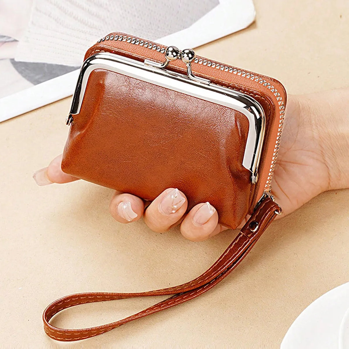 Brown leather clutch with a strap held by a hand on a beige surface