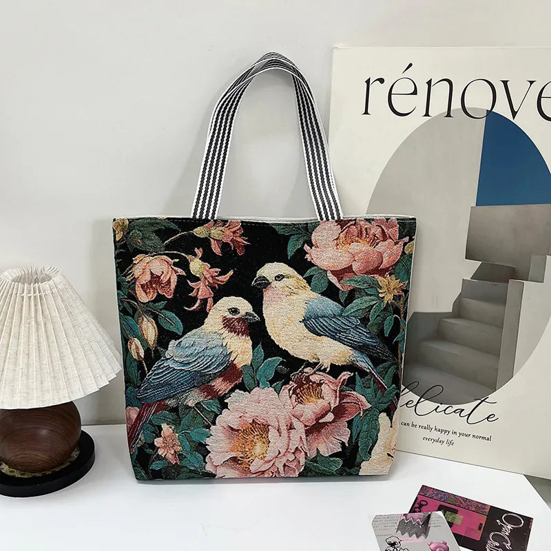 Tote bag with floral and bird design on a surface with a magazine and small lamp.