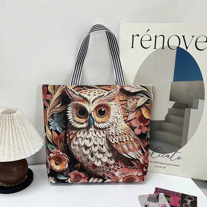 Tote bag with owl design on a surface next to a magazine and small lamp.